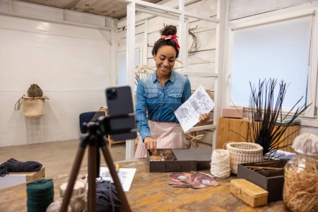 Téléchargez les photos : Atelier en ligne.Jeune femme avec chignon à cheveux présentant de nouveaux sacs faits à la main sur un atelier - en image libre de droit