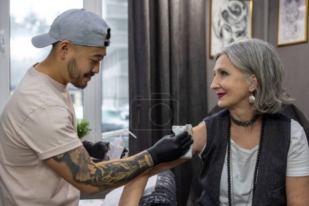 Téléchargez les photos : Dans le salon de tatouage. Maître de tatouage préparant le client pour une session de tatouage - en image libre de droit