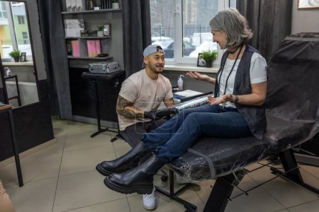 Téléchargez les photos : Dans le salon de tatouage. Femme aux cheveux gris se préparant pour la session de tatouage - en image libre de droit