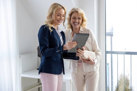 Téléchargez les photos : Agent immobilier professionnel joyeux montrant un accord d'achat à son sourire heureux client féminin - en image libre de droit