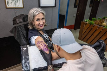Foto de En el salón de tatuajes. Tatuaje maestro dibujo tatuaje en mujer brazo - Imagen libre de derechos