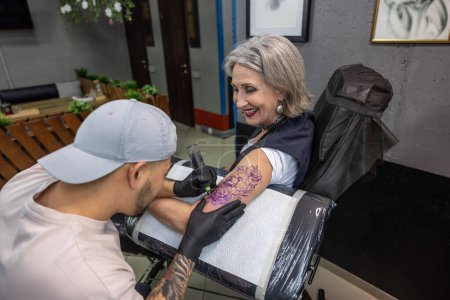 Téléchargez les photos : Dans le salon de tatouage. Tatouage maître dessin tatouage sur bras de femme - en image libre de droit