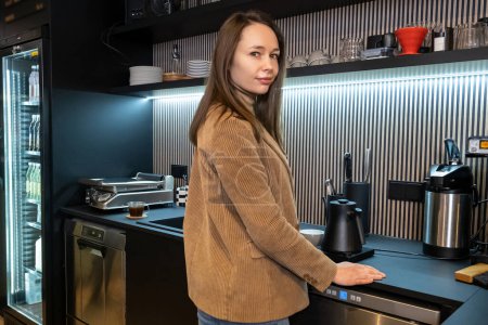 Téléchargez les photos : Calme jeune travailleur de café caucasien appuyé sur le comptoir devant une bouilloire électrique - en image libre de droit