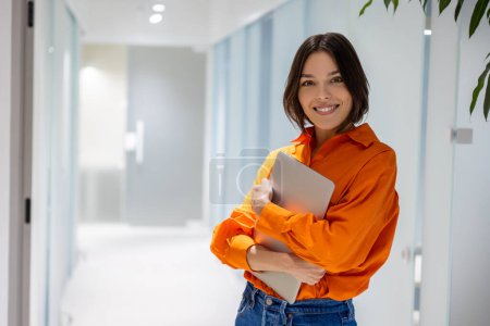 Photo for Smiling stylish young Caucasian woman with the laptop in the hands standing in the corridor - Royalty Free Image