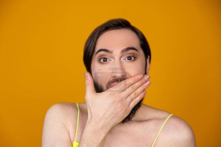 Photo for Shocked astonished bearded transsexual person being amazed and excited covering mouth with hand posing isolated over orange background - Royalty Free Image