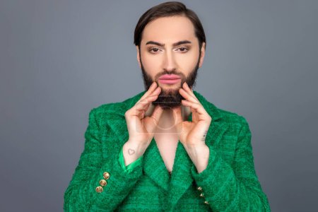 Photo for Handsome beautiful dark haired transsexual person wearing green jacket showing his well-groomed beard posing isolated over gray background - Royalty Free Image