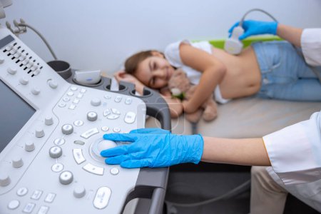 Foto de Médico que lleva a cabo el examen por ultrasonido de los riñones al niño en la clínica, diagnóstico de pielonefritis infantil. - Imagen libre de derechos