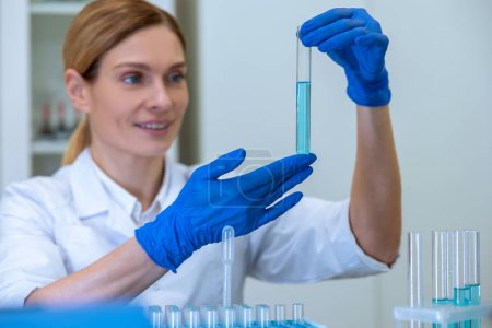 Photo for Blonde successful woman researcher working with medical samples, holding test tube with blue liquid, making microbiology investigating in laboratory. - Royalty Free Image