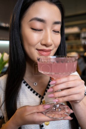 Foto de Retrato de una joven asiática joven agradable inhalando aroma de una bebida en sus manos - Imagen libre de derechos