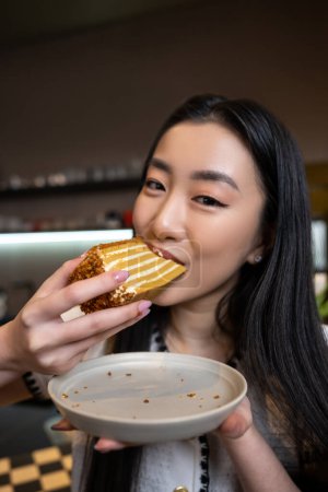 Téléchargez les photos : Portrait d'une femme brune tenant une assiette vide dans sa main mordant une tranche de gâteau - en image libre de droit
