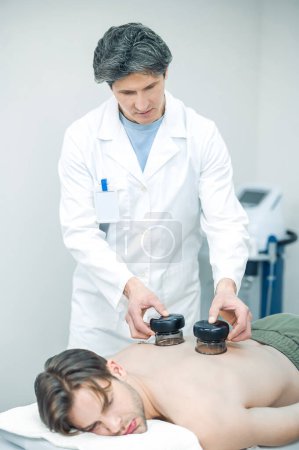 Photo for Medical cups. Experienced therapist putting medical cups on patients back - Royalty Free Image