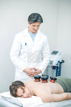 Foto de Tratamiento de espalda. Doctor poniendo tazas médicas en sus pacientes de vuelta - Imagen libre de derechos