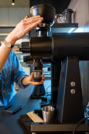 Foto de Foto recortada de un empleado experto café moliendo granos de café con un molinillo de café eléctrico - Imagen libre de derechos