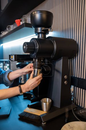 Foto de Foto recortada de un trabajador experimentado de la cafetería moliendo granos de café con un molinillo de café eléctrico - Imagen libre de derechos