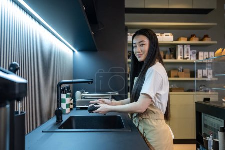 Téléchargez les photos : Vue latérale d'un sourire heureux jeune employé de café mignon séchant ses mains avec une serviette - en image libre de droit