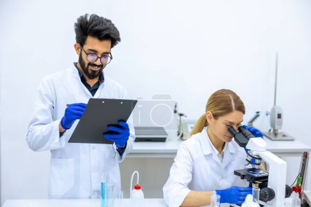 Photo for Woman and man scientists in lab coat making notes after doing sample test in laboratory, professional worker analyzes received data together. - Royalty Free Image