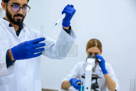 Téléchargez les photos : Scientifiques féminins et masculins utilisant une pipette avec éprouvette dans un laboratoire de science médicale, examiner un échantillon médical au microscope - en image libre de droit