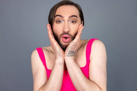 Téléchargez les photos : Incroyable surpris brunette transsexuelle portant haut rose voit quelque chose d'étonnant garde les paumes sur les joues en disant wow posant isolé sur fond gris - en image libre de droit