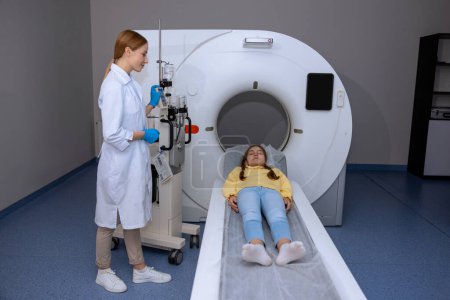Téléchargez les photos : Petite fille patiente allongée sur une longue table médicale lors d'une IRM à l'hôpital, médecin pratiquant la tomographie d'un enfant dans une clinique. - en image libre de droit