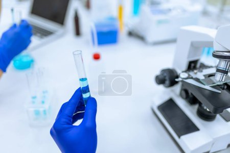 Foto de Científico irreconocible con guantes de goma azul examinando líquido en tubo de ensayo en laboratorio. - Imagen libre de derechos