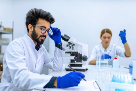 Photo for Health care researchers working in science laboratory, microscoping, making notes of his investigation, working together with colleague, making diagnostic. - Royalty Free Image