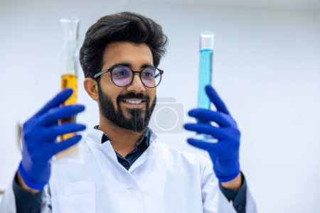Photo for Scientist examining liquid in test tube in laboratory, researcher wearing lab coat and rubber gloves holding glass flask with yellow and blue liquid in hands. - Royalty Free Image
