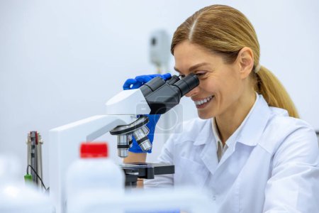 Téléchargez les photos : Femme scientifique médicale regardant au microscope, effectuant l'analyse de l'échantillon d'essai, ambitieuse spécialiste de la biotechnologie travaillant en laboratoire. - en image libre de droit