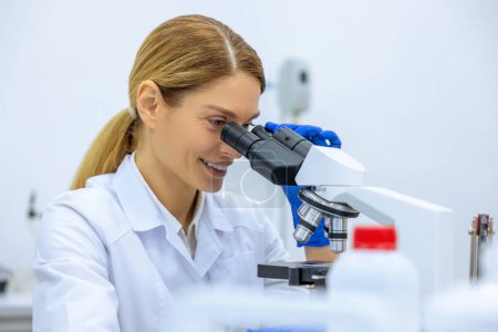 Téléchargez les photos : Femme scientifique médicale regardant au microscope, effectuant l'analyse de l'échantillon d'essai, ambitieuse spécialiste de la biotechnologie travaillant en laboratoire. - en image libre de droit