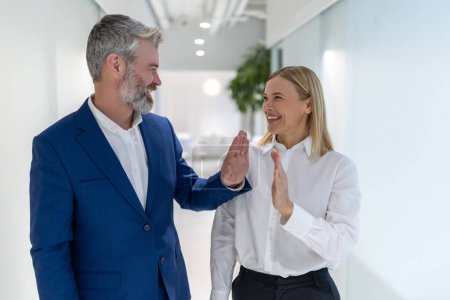Photo for Joyous businessman and a businesswoman giving each other the high five in the office corridor - Royalty Free Image