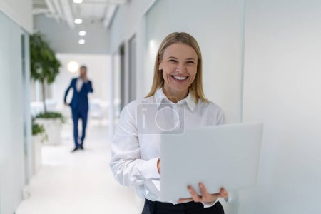 Photo for Joyful elegant attractive young female entrepreneur typing on the portable computer in the office corridor - Royalty Free Image