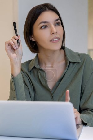 Foto de Trabajadora corporativa joven y pensativa con un bolígrafo en la mano sentada en el monitor de la computadora - Imagen libre de derechos