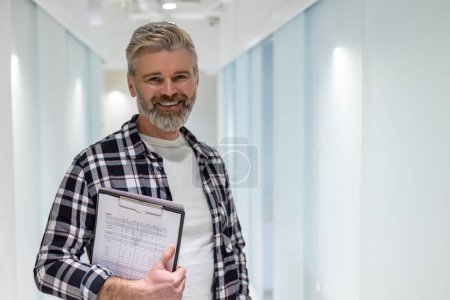 Foto de Retrato en la cintura de un trabajador de oficina alegre con el portátil y documentos en la mano de pie en el pasillo - Imagen libre de derechos