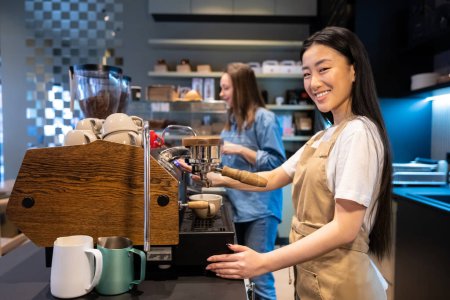 Foto de Barista sonriente haciendo café con la cafetera espresso en un café en presencia de su colega - Imagen libre de derechos