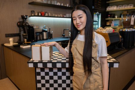 Foto de Sonriendo contenta atractiva trabajadora de pelo largo apoyada contra el mostrador de servicio en una cafetería - Imagen libre de derechos