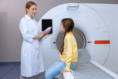 Photo for Medical equipment. Female doctor and little girl patient in MRI room in hospital, talking before diagnostics. - Royalty Free Image