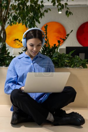 Photo for Smiling focused cute young dark-haired female in the wireless headphones working on the portable computer - Royalty Free Image
