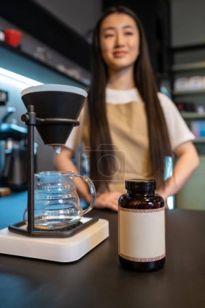 Foto de Primer plano de una cafetera y una botella de plástico en el mostrador de la barra y un barista pensativo en el fondo - Imagen libre de derechos