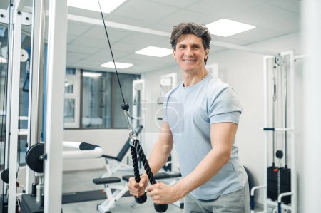 Photo for Rehabilitating exercises. Smiling dark-haired man standing near training device - Royalty Free Image