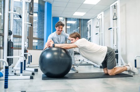 Photo for Rehabilitation. Experienced instructor assisting a man in a rehabilitation workout - Royalty Free Image