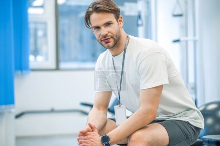 Photo for In a gym. Young man in sportswear sitting on a training device in a gym - Royalty Free Image