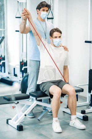 Photo for Rehabilitation. Doctor and patient in protective masks having a workout in a rehabilitation center - Royalty Free Image