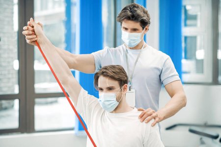 Foto de Rehabilitación. Médico y paciente con máscaras protectoras haciendo ejercicio en un centro de rehabilitación - Imagen libre de derechos
