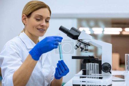 Téléchargez les photos : Attrayant scientifique positif examinant liquide dans une éprouvette en laboratoire, faisant des recherches sur l'ADN, posant à son lieu de travail. - en image libre de droit