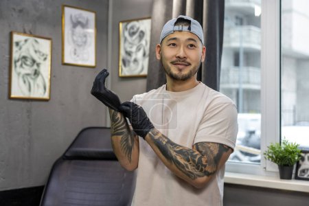 Téléchargez les photos : Dans le salon de tatouage. Jeune homme asiatique portant des gants - en image libre de droit