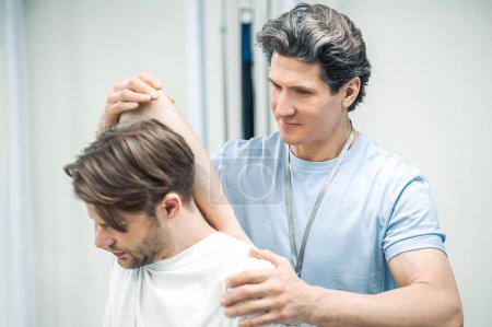 Photo for Rehabilitation. Male manual therapist helping his patient to work out the shoulder-joint - Royalty Free Image
