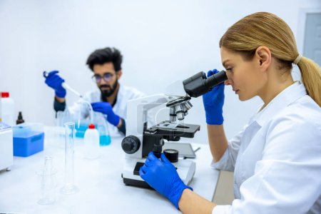 Photo for Researchers man and woman working with lab microscope for research project in hospital laboratory room, quality control expert looking specimen. - Royalty Free Image