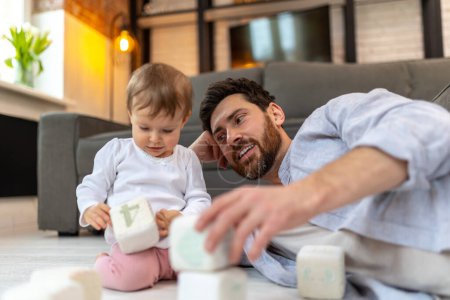 Photo for Bearded father playing with toddler child on floor with cubes in home interior. - Royalty Free Image