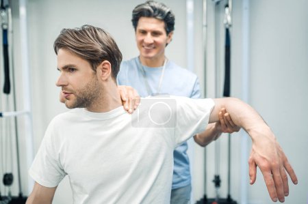 Téléchargez les photos : Exercice de récupération. Physiothérapeute masculin travaillant avec un patient et regardant invloved - en image libre de droit