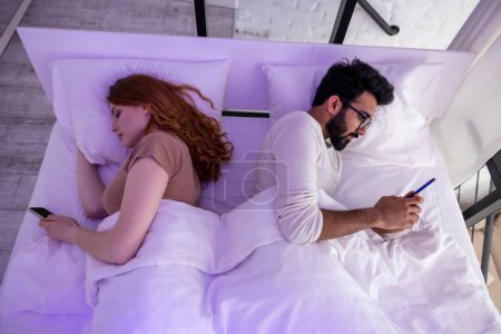 Téléchargez les photos : Jeune couple au lit en utilisant le téléphone couché dos à l'autre
. - en image libre de droit