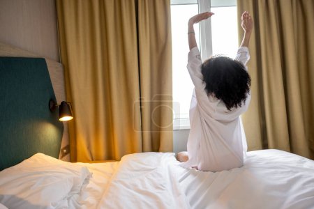 Téléchargez les photos : Bonjour. Jolie femme aux cheveux bouclés en peignoir blanc dans un hôtel le matin - en image libre de droit